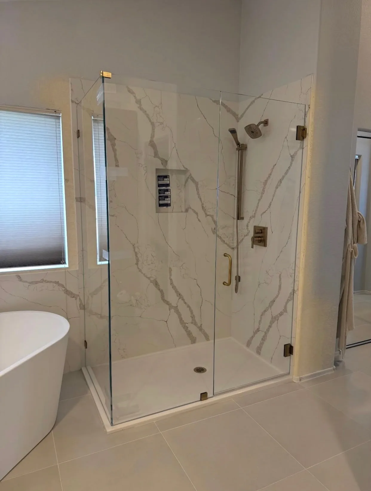 Master bathroom with a frameless glass shower enclosure, marble-look quartz walls, and brushed brass fixtures