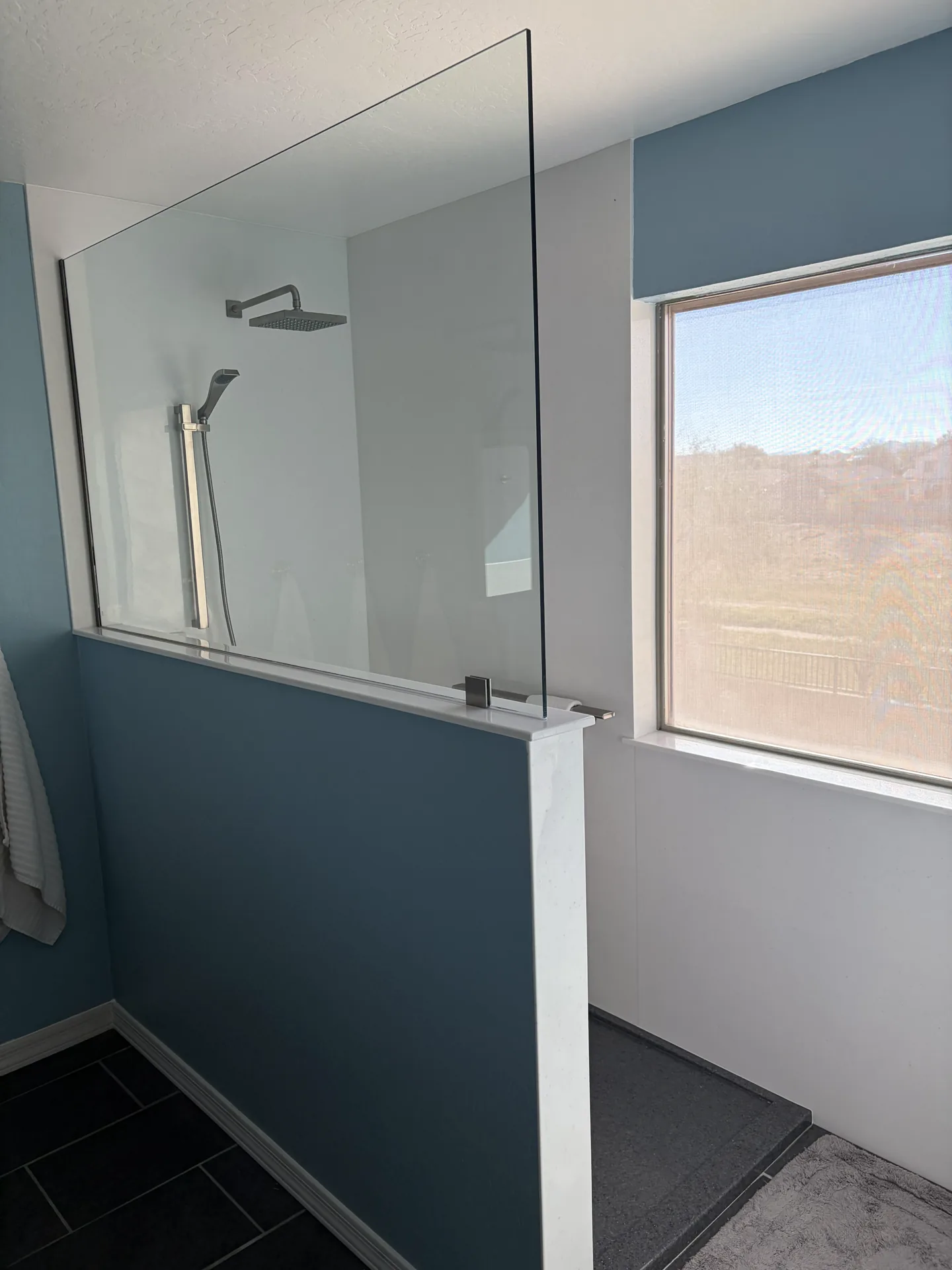 Doorless walk-in shower with a glass partition, white low-maintenance panels, and a rain shower head
