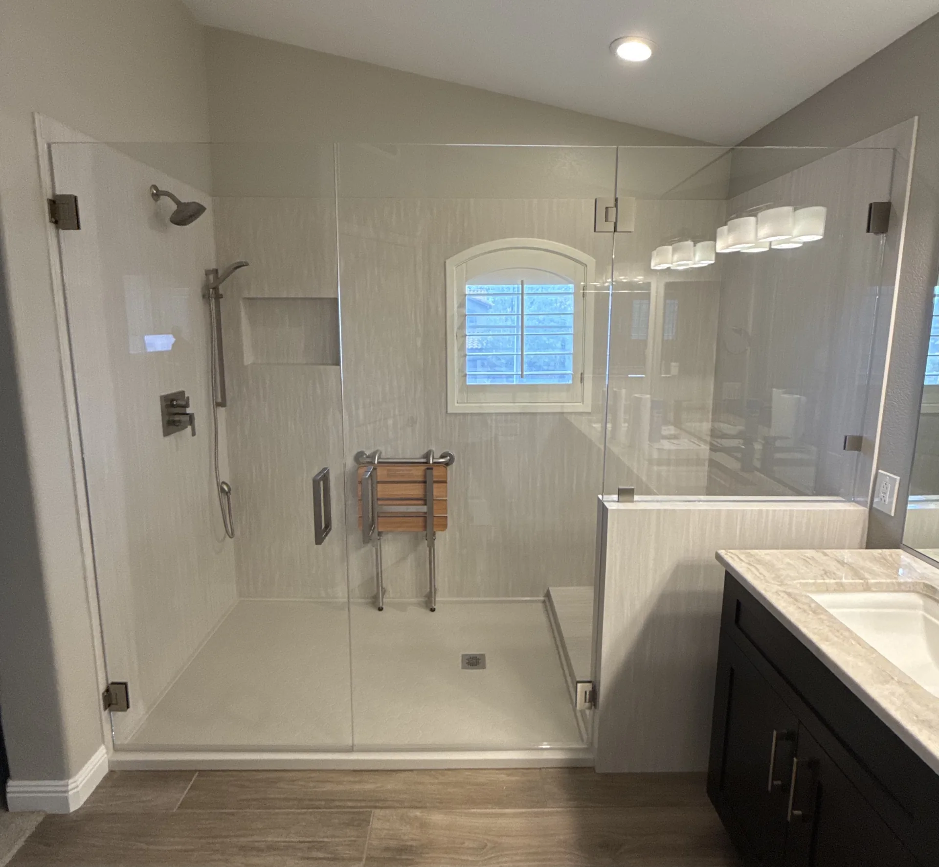 Walk-in shower conversion with a frameless glass enclosure, low-maintenance panels, a fold-down teak seat, and grab bars by Orange Cactus Remodeling