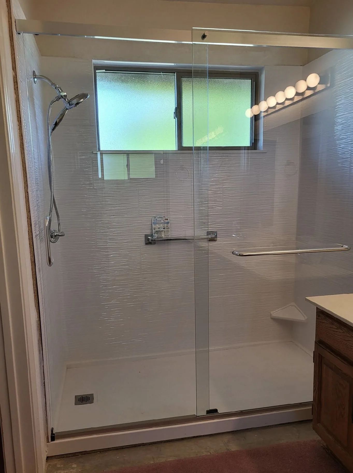 Walk-in shower with white textured low-maintenance wall panels, a sliding glass door, and grab bars