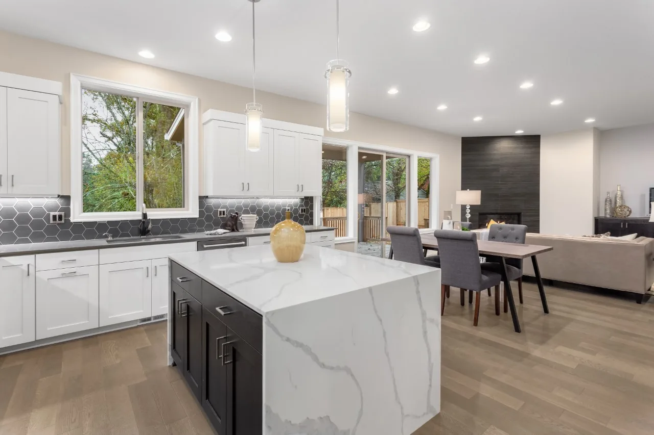 Full kitchen remodel with white cabinetry, a dark island, waterfall quartz countertops, and open-concept living
