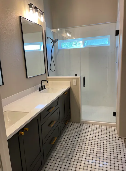 Finished bathroom remodel with a dark double vanity, frameless glass shower, and brass fixtures by Orange Cactus Remodeling in Chandler, AZ