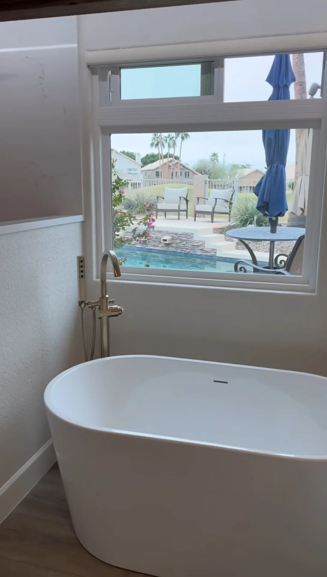 Freestanding soaking tub with a floor-mounted tub filler beside a picture window