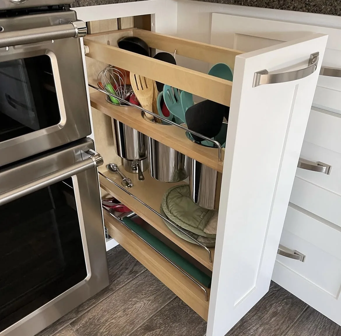 Custom pull-out base cabinet organizer with utensil and storage inserts next to a stainless double oven