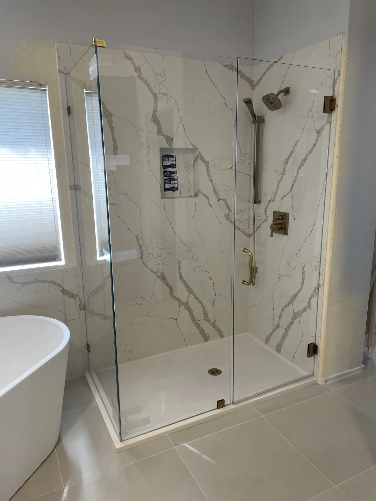 Full bathroom remodel with a frameless glass shower, marble-look quartz walls, freestanding tub, and brass fixtures by Orange Cactus Remodeling in Chandler, AZ