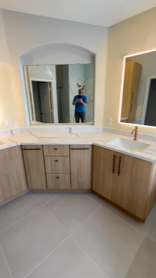 Bathroom remodel with a corner double vanity, wood-tone cabinetry, and lit mirrors by Orange Cactus Remodeling, serving Sun Lakes, AZ
