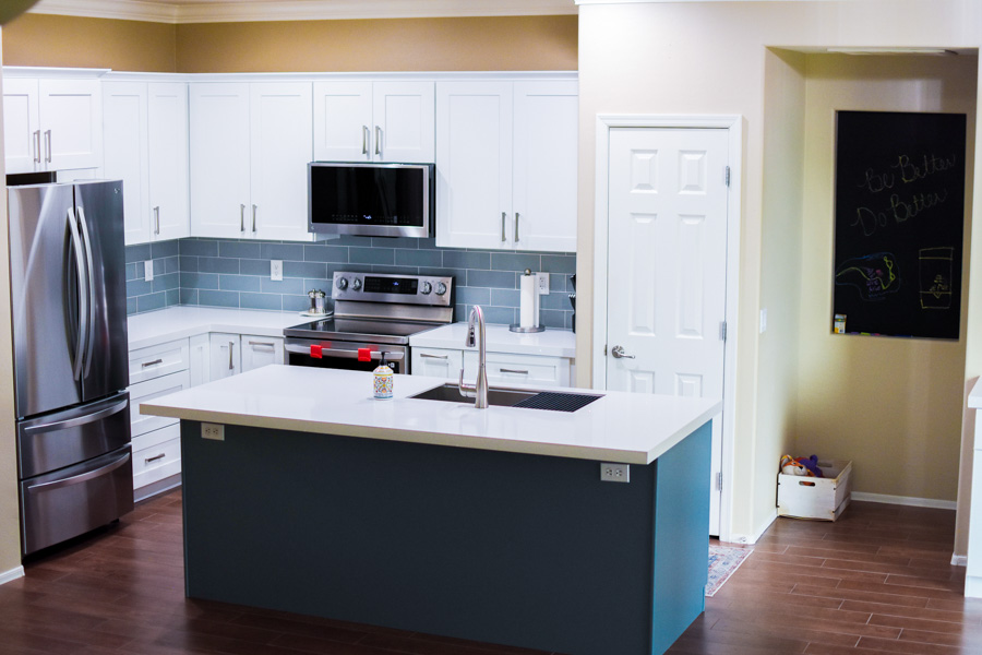 Open-concept kitchen with white cabinets, a navy island, and stainless appliances