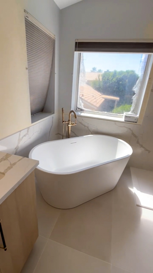 Freestanding soaking tub beside a window with a marble-look surround and a brushed-gold filler, remodeled by Orange Cactus Remodeling, serving Sun Lakes, AZ