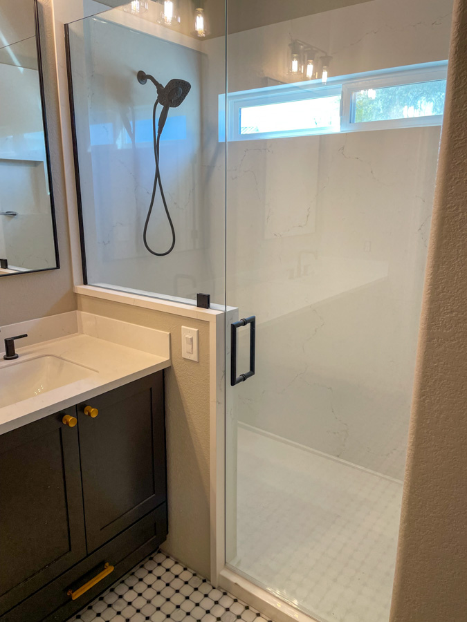 Finished bathroom remodel with a marble-look walk-in shower, dark vanity, and brass accents